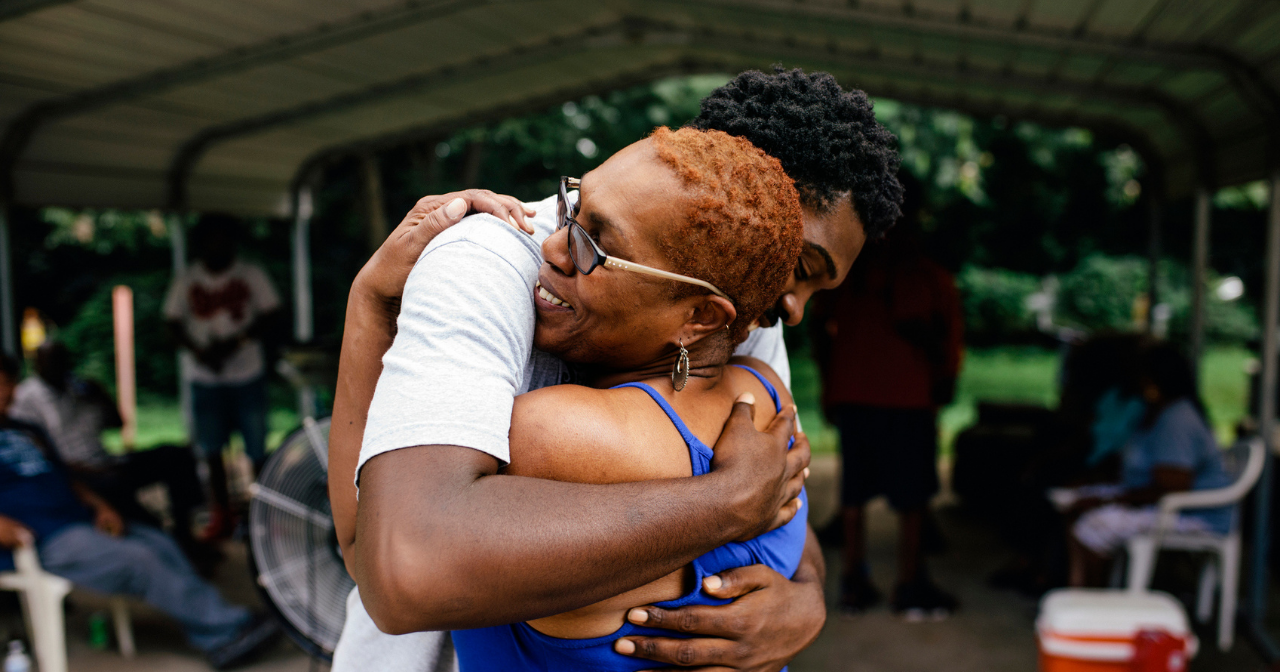 A Black woman hugs her son outdoors. 