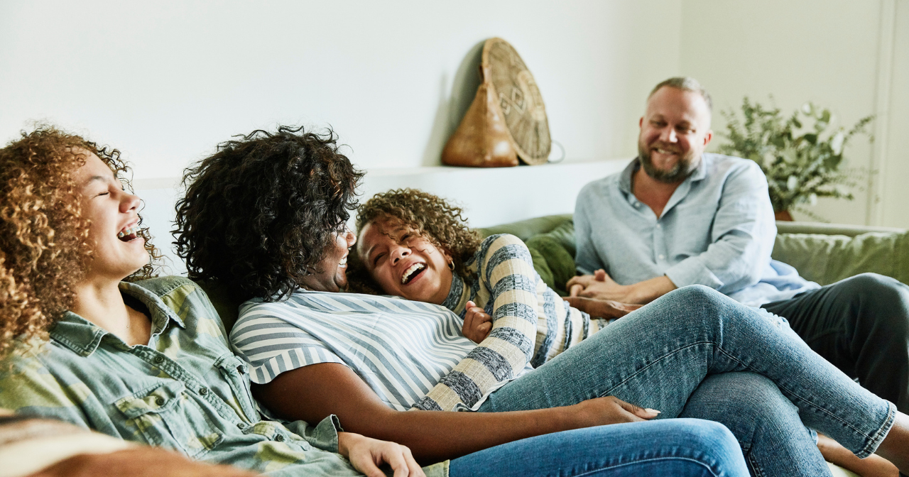 A family with preteen children laugh together on the sofa. 