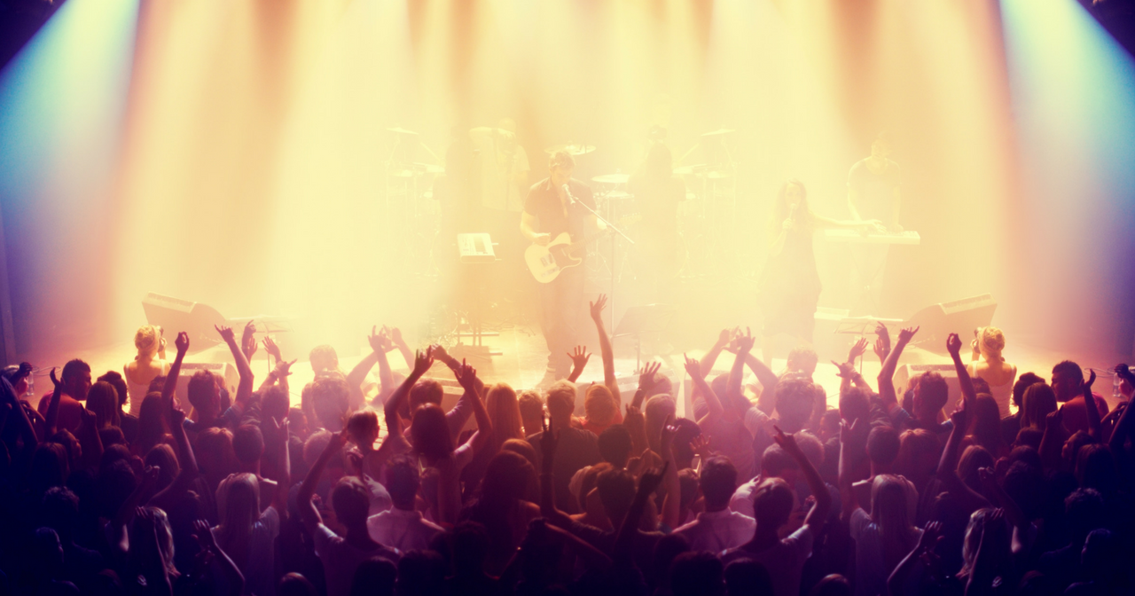 An image of a concert and the audience with their hands up