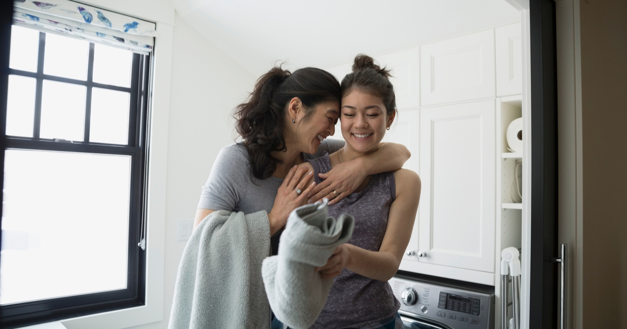 A mother hugs her teen as she folding laundry.