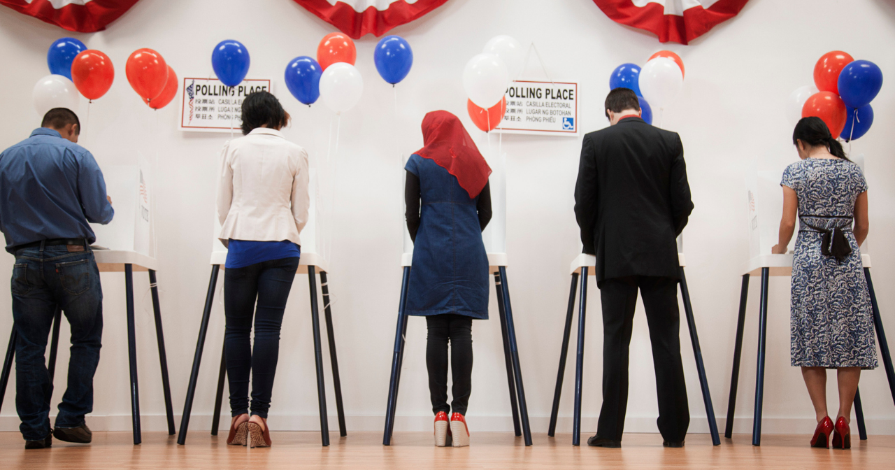 Two men and three women stand at voting booths and cast their ballots. 