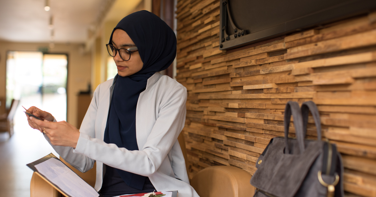 A provider wearing a hijab while sitting on a bench and reviewing information. 