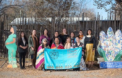 A group photo of Tewa women holding a banner for the organization. 