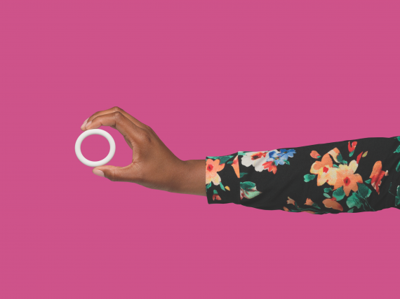 A hand with a floral sleeve holds the Annovera ring against a pink background. 