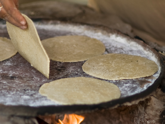 A hand flips a tortilla on a plate over a fire. 
