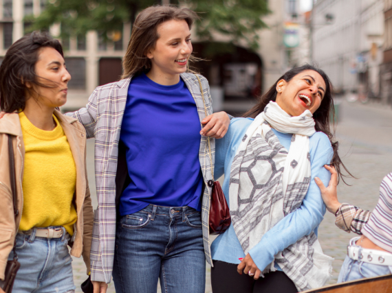 Four friends stand on the street and laugh together. 