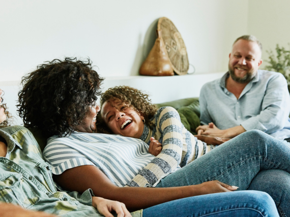 A family with preteen children laugh together on the sofa. 