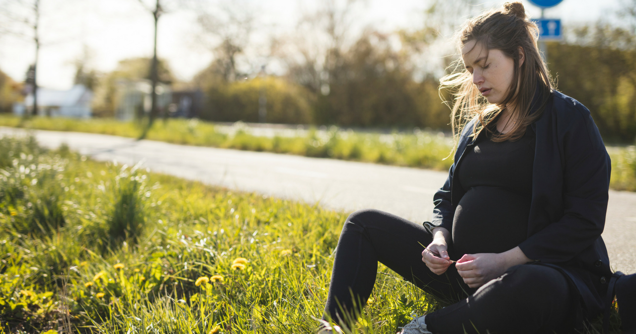 A pregnant woman sits by a road