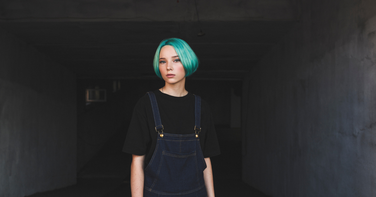 a teen with blue hair stands in an empty room