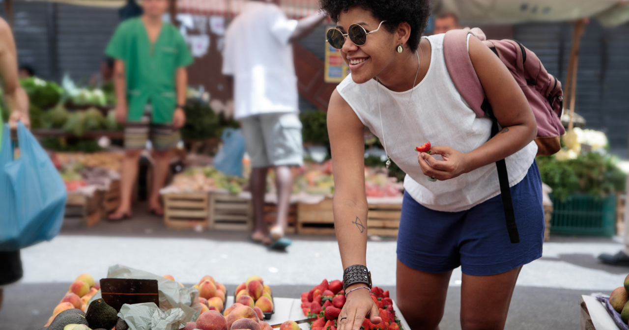 a young black woman happily looks at fruit at a farmer's market