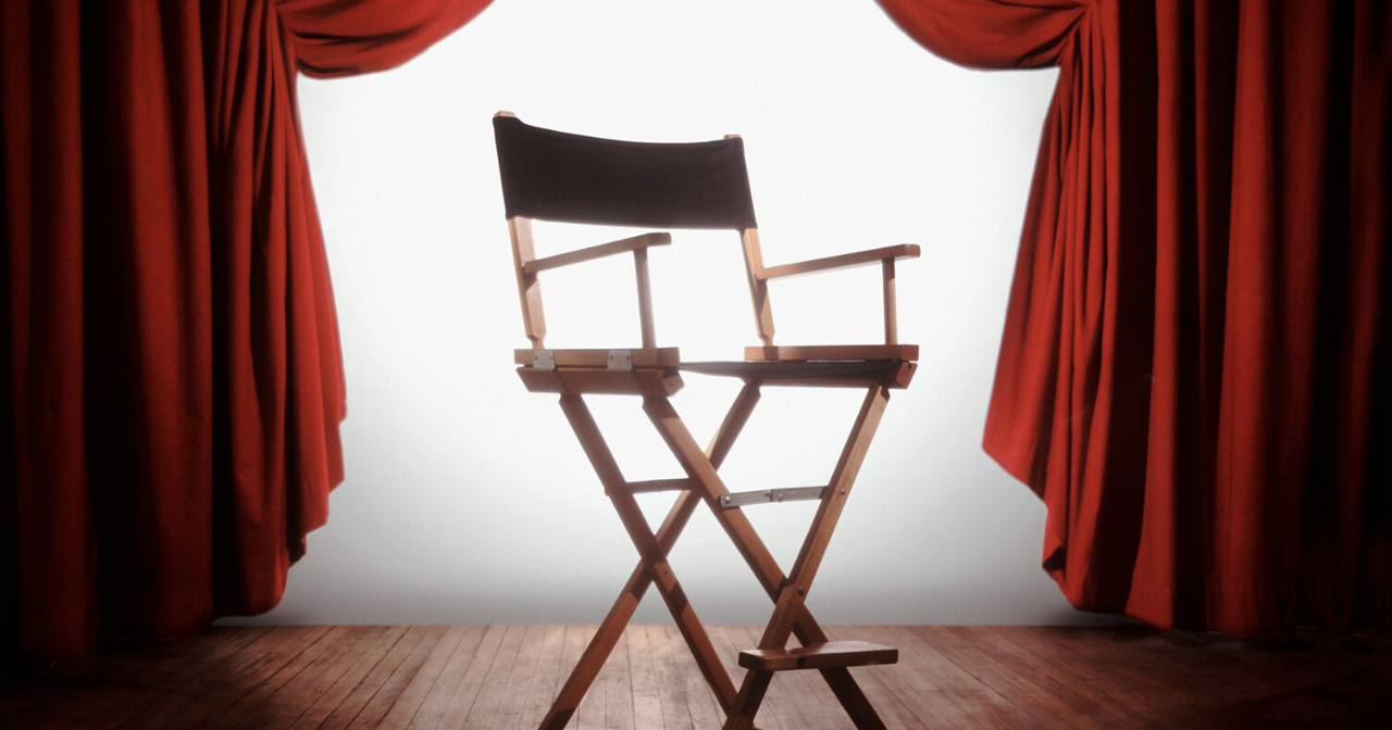 A classic director's chair sits backlit between two red velvet curtains. 