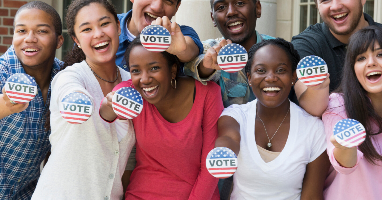 A group of teens smile and hold out red, white, and blue buttons that read, "Vote."