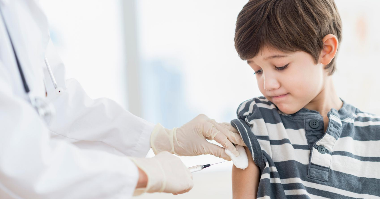 A young boy looks down as he is vaccinated by a provider. 