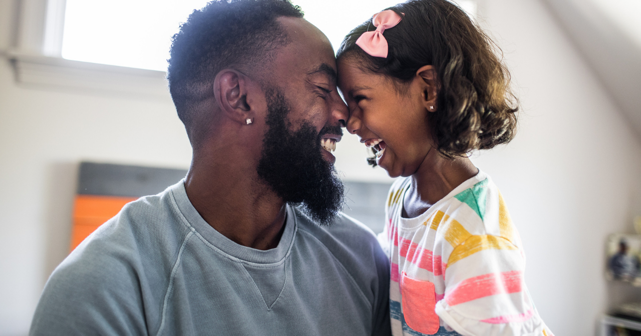 A Black father and his young daughter smile and hug. 