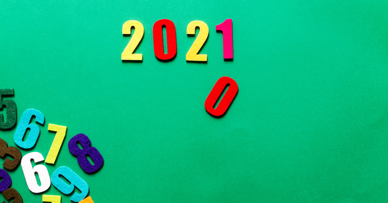Refrigerator magnets in the shape of numbers sit on a green background. 2021 is spelled out with a zero falling down under where the 1 sits. 