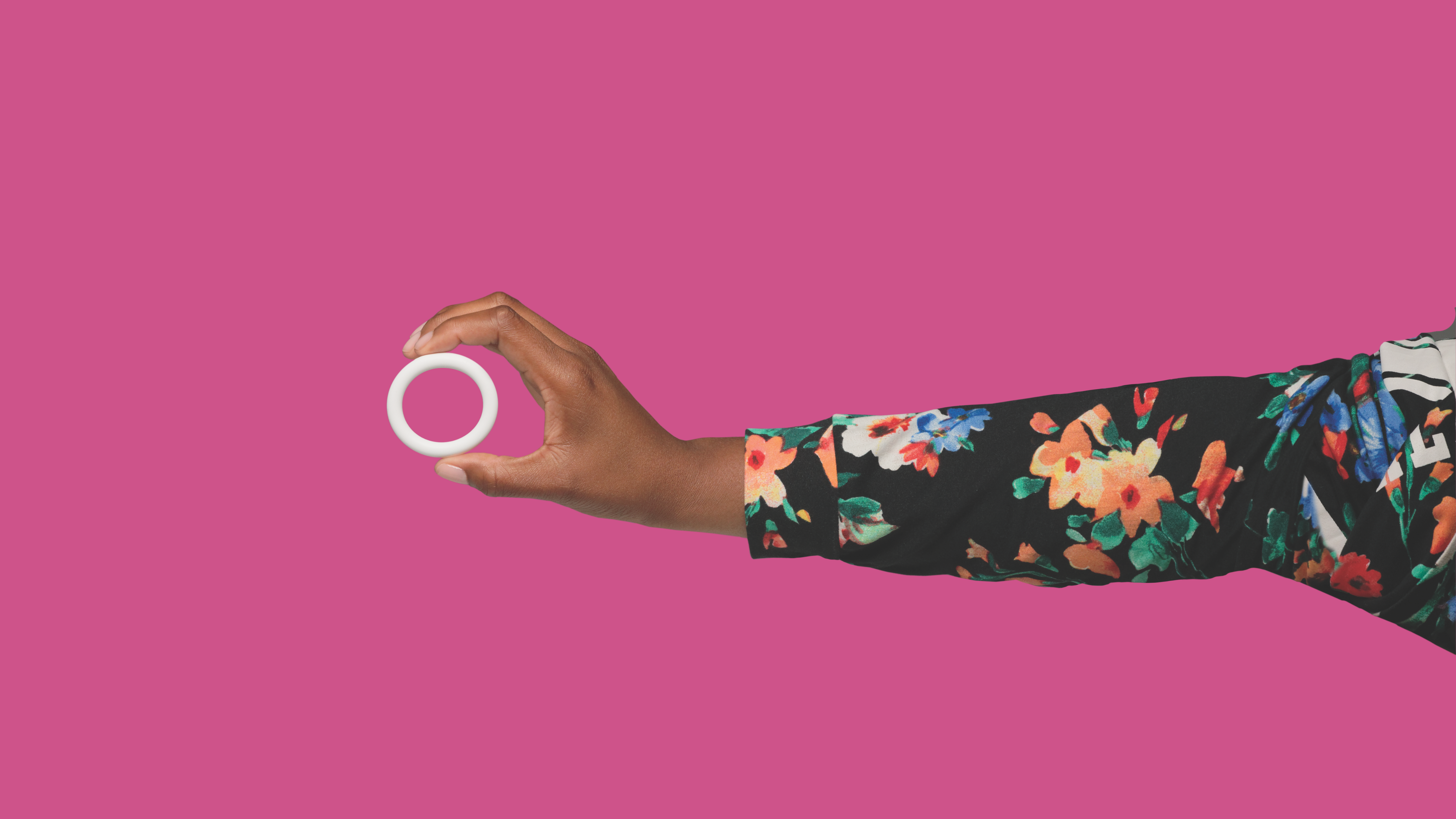 A hand with a floral sleeve holds the Annovera ring against a pink background. 