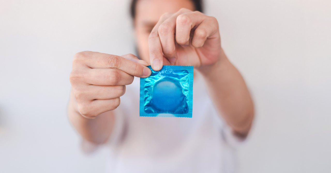 An out of focus woman holds a condom in its wrapped and begins to open it. 
