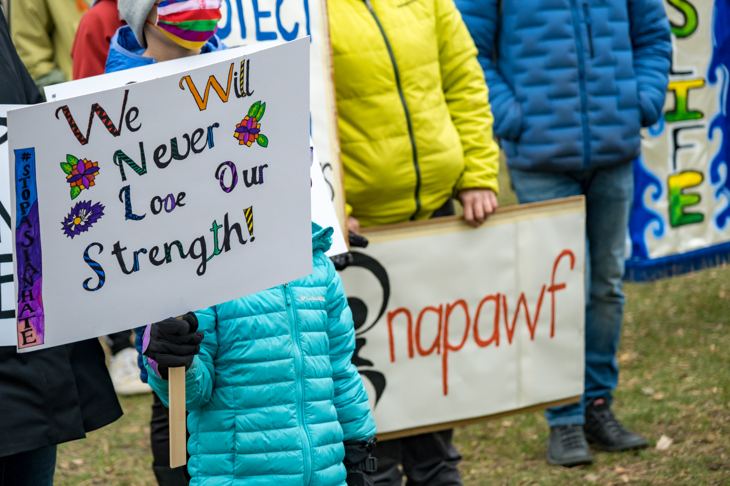 A photo of people holding signs that read, "We will never lose our strength!" and "NAPAWF"