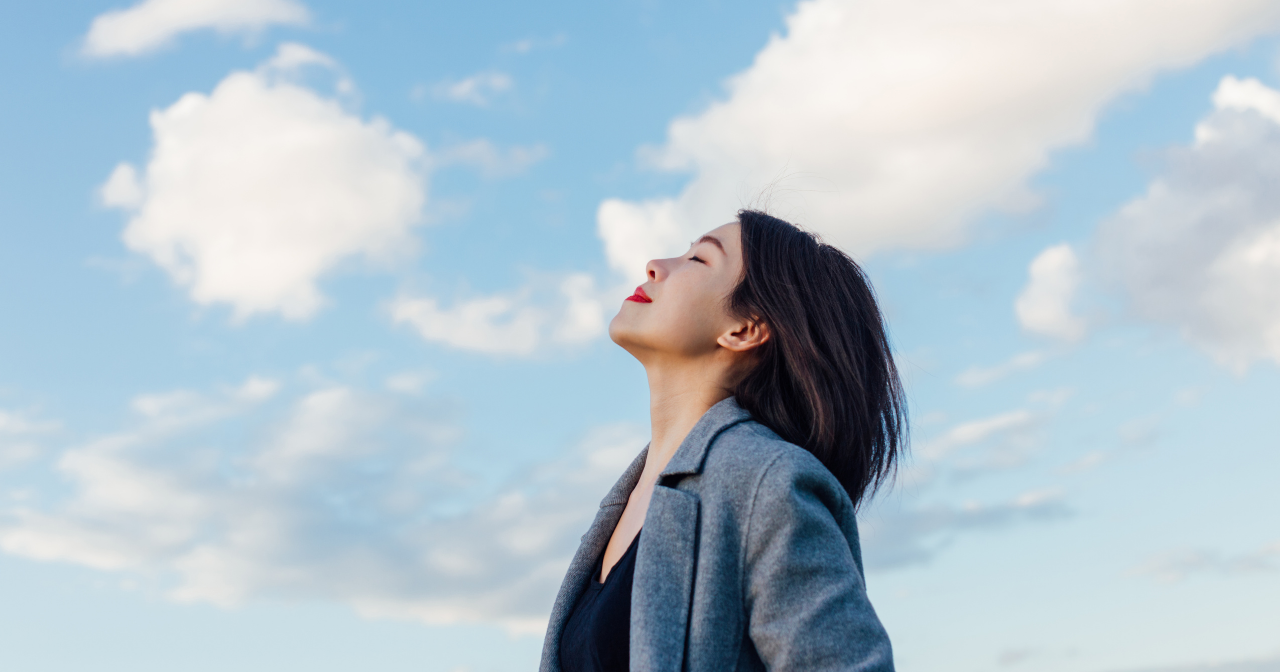 A woman looks up at the sky with a contented smile and closed eyes. 