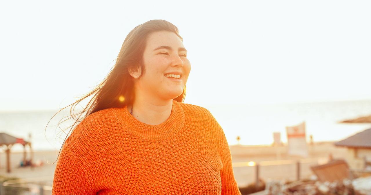 A woman stands on a rooftop at sunset and smiles. 