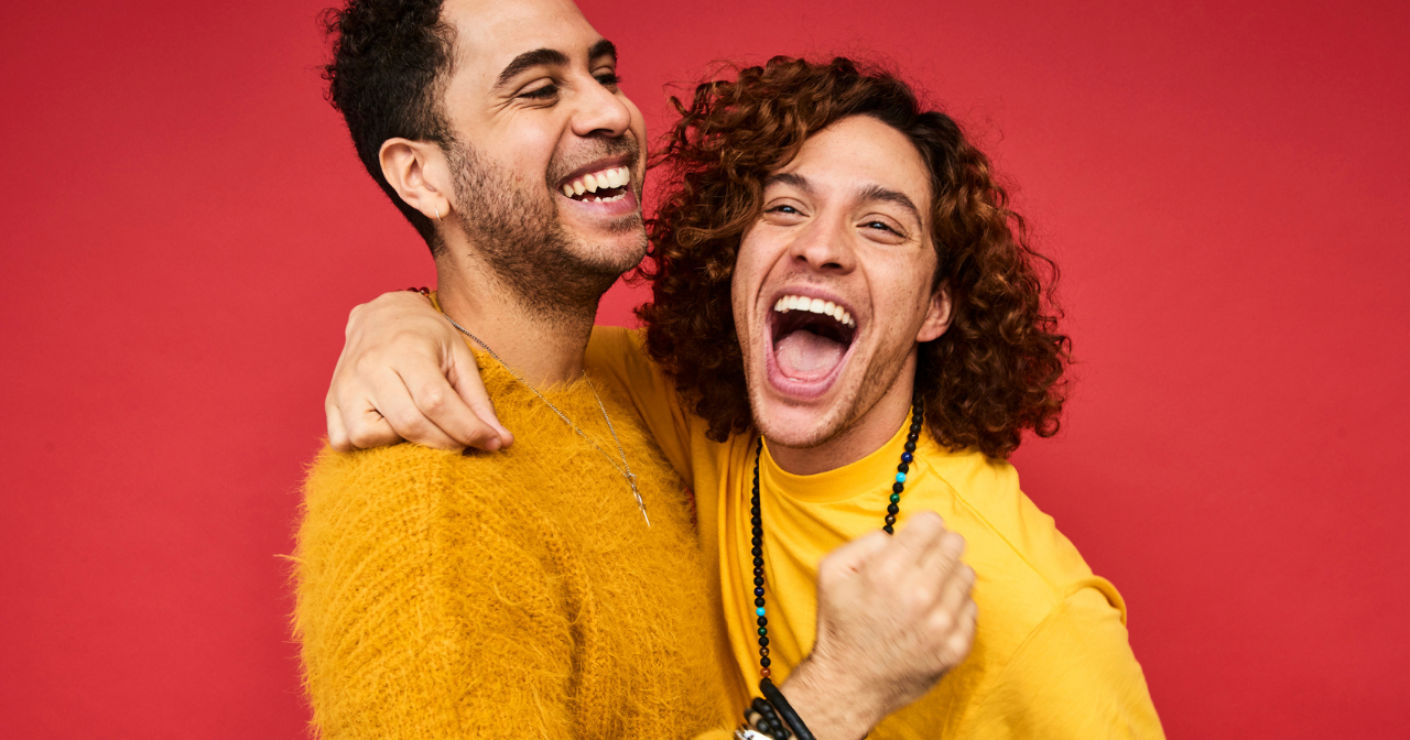 Two men in a relationship laugh and hug for a photo. 