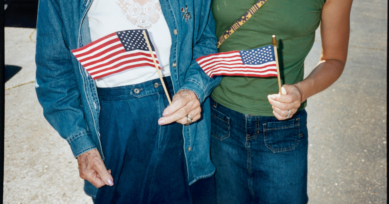 A photo of the torsos of two women standing on the street holding American flags. 