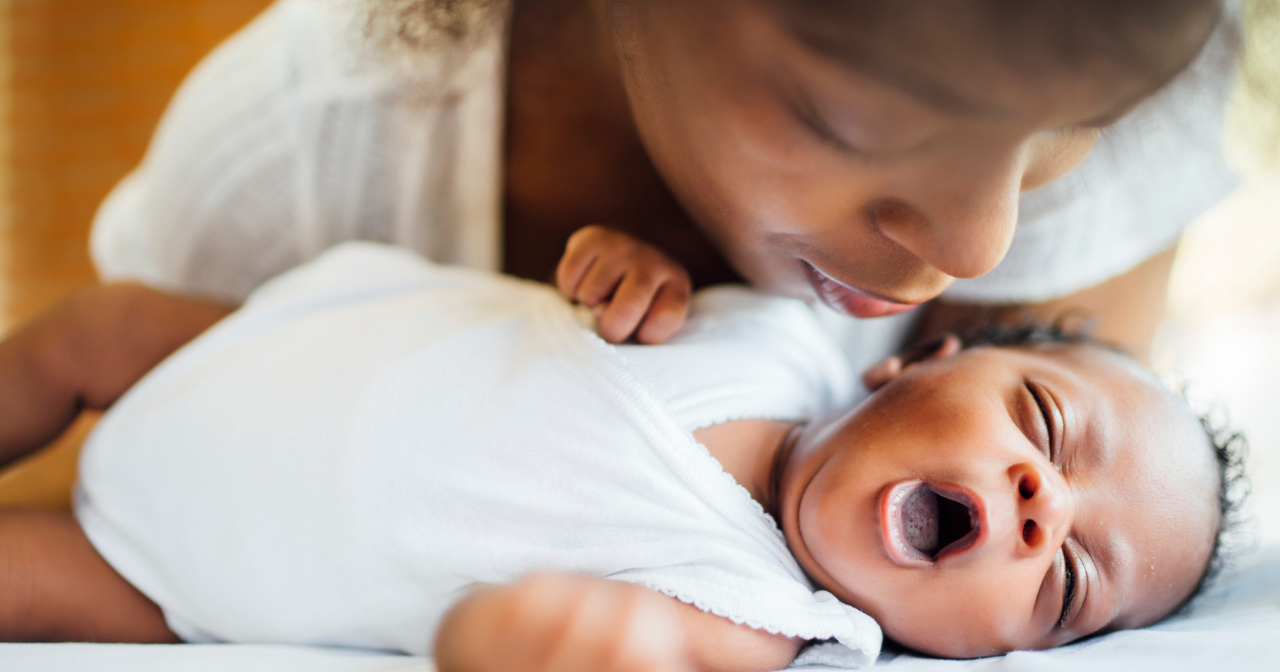 A Black mother kisses her newborn's head while the baby yawns. 