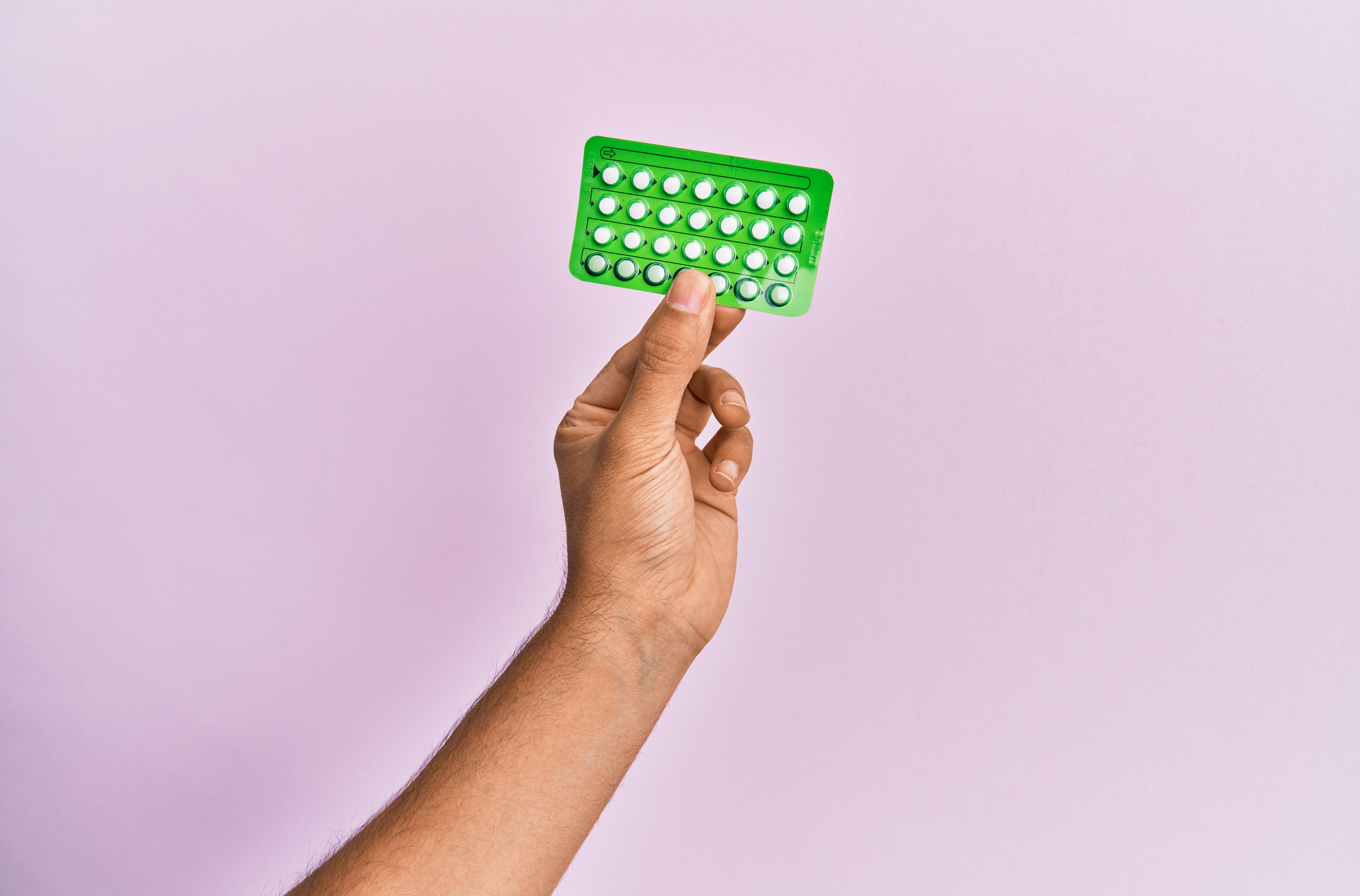 A hand holds a generic pill pack against a purple background. 