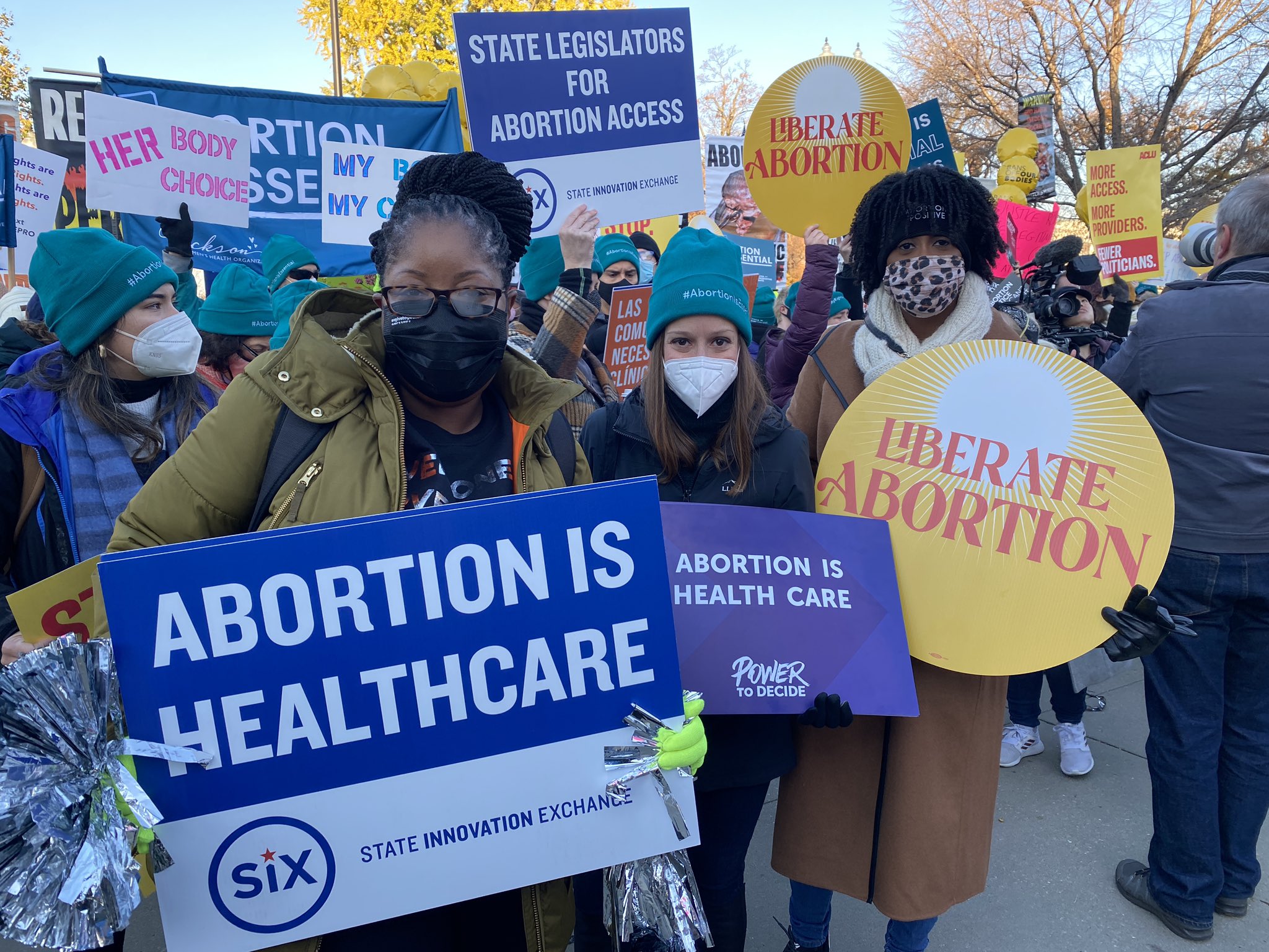 Three people holding signs at a rally supporting abortion access. 