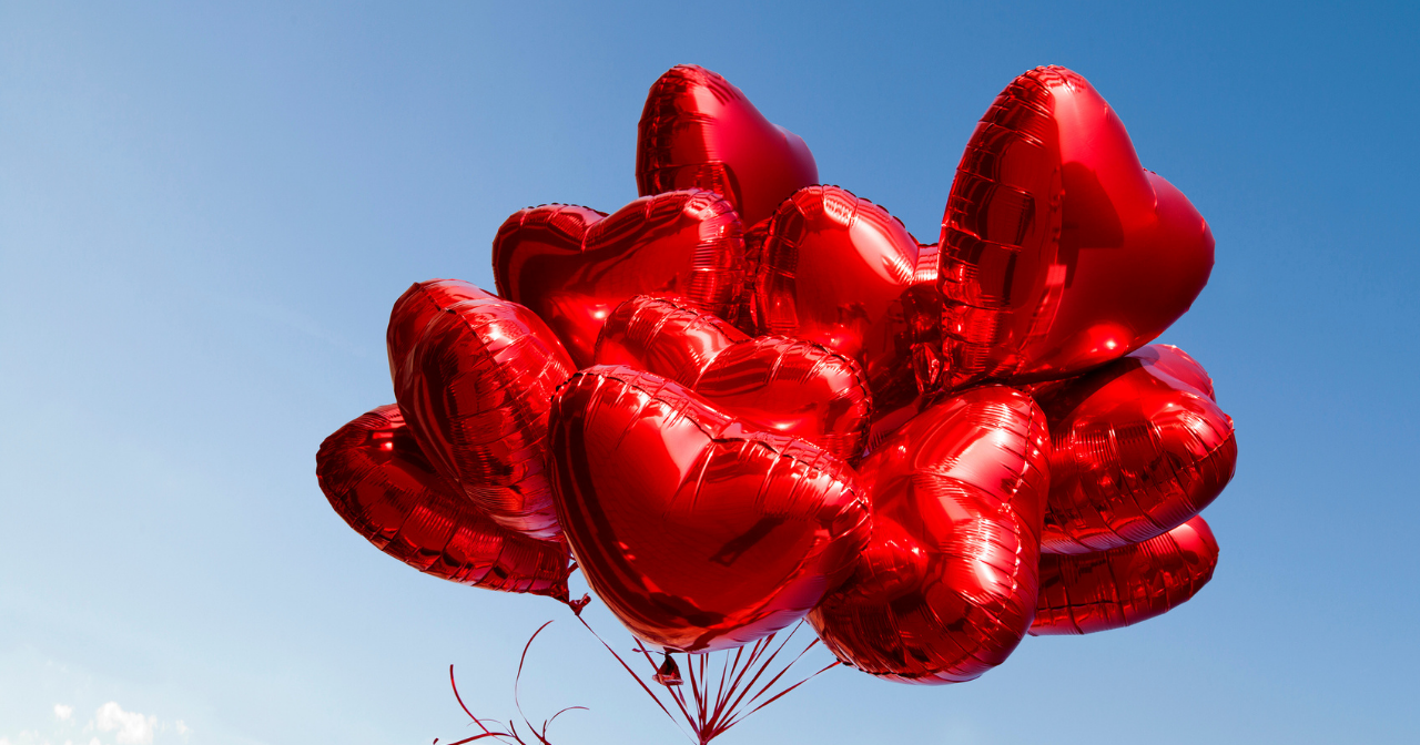 A large bunch of heart balloons against a bright blue sky. 