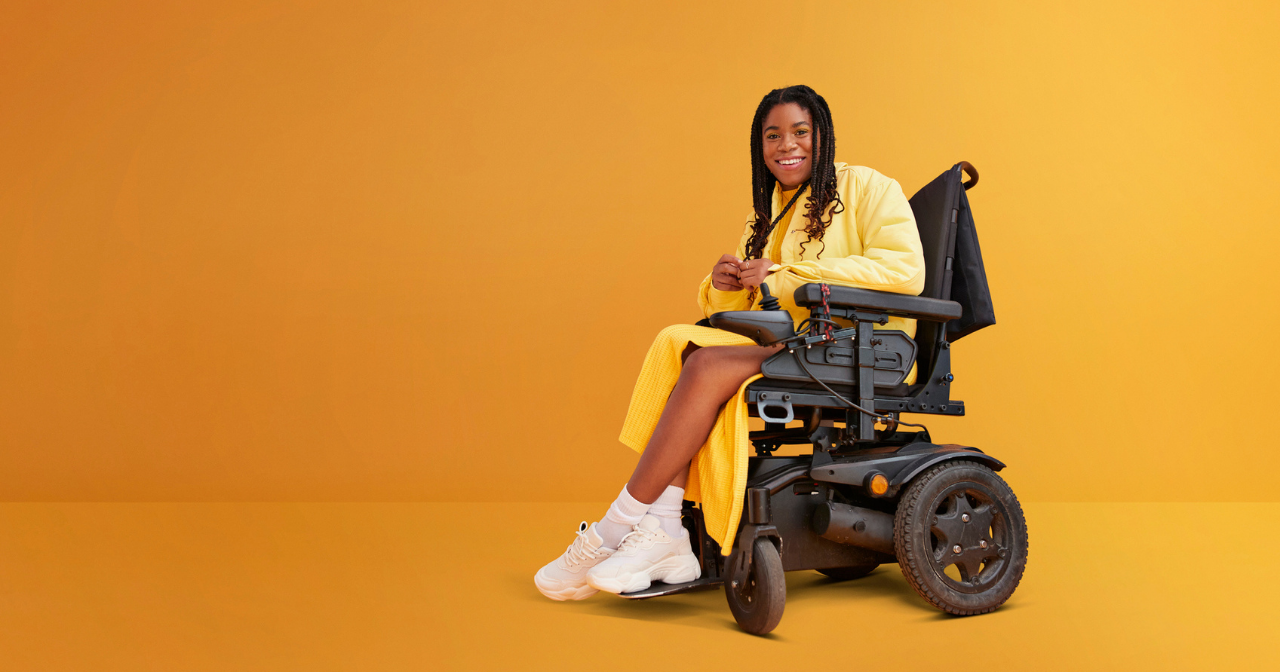 Against a yellow background, a Black woman dressed in yellow and sitting in a wheelchair smiles broadly.