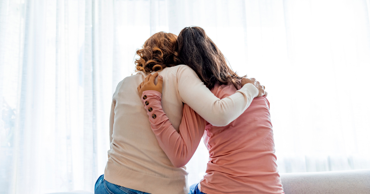A photo of the backs of a mom and daughter hugging. 