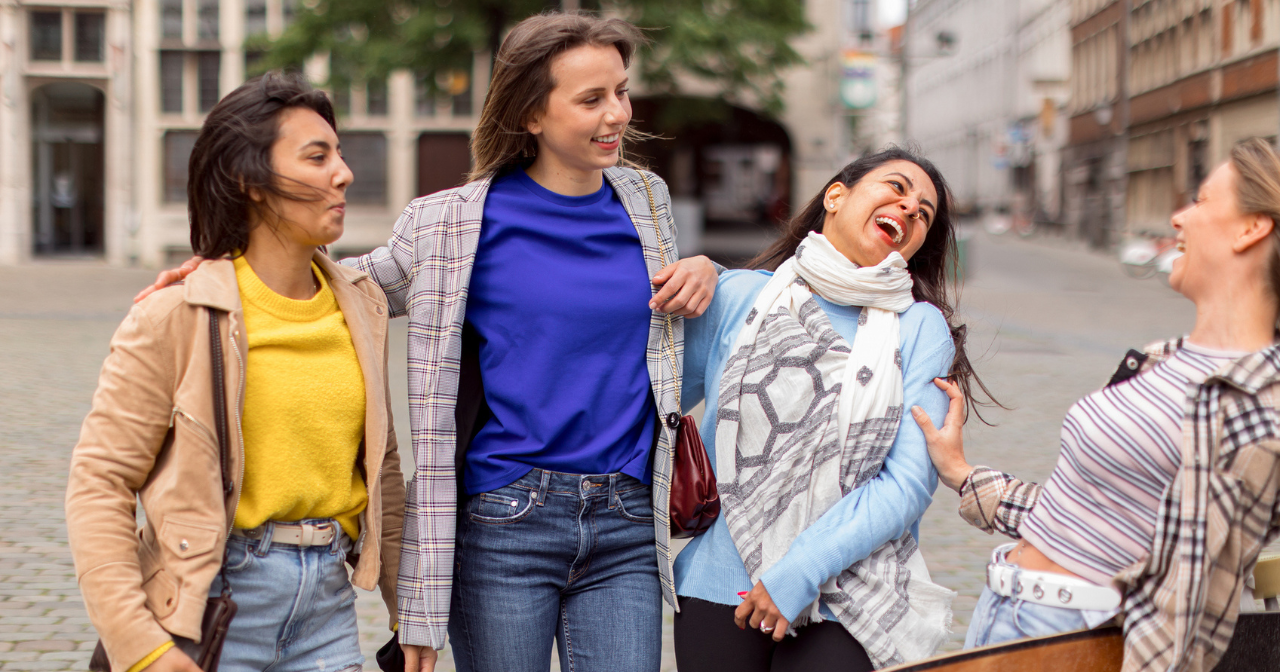 Four friends stand on the street and laugh together. 