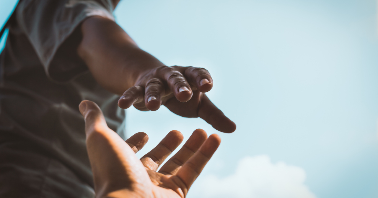 One person's hand reaches down to grasp another person's hands with a blue sky in the background.