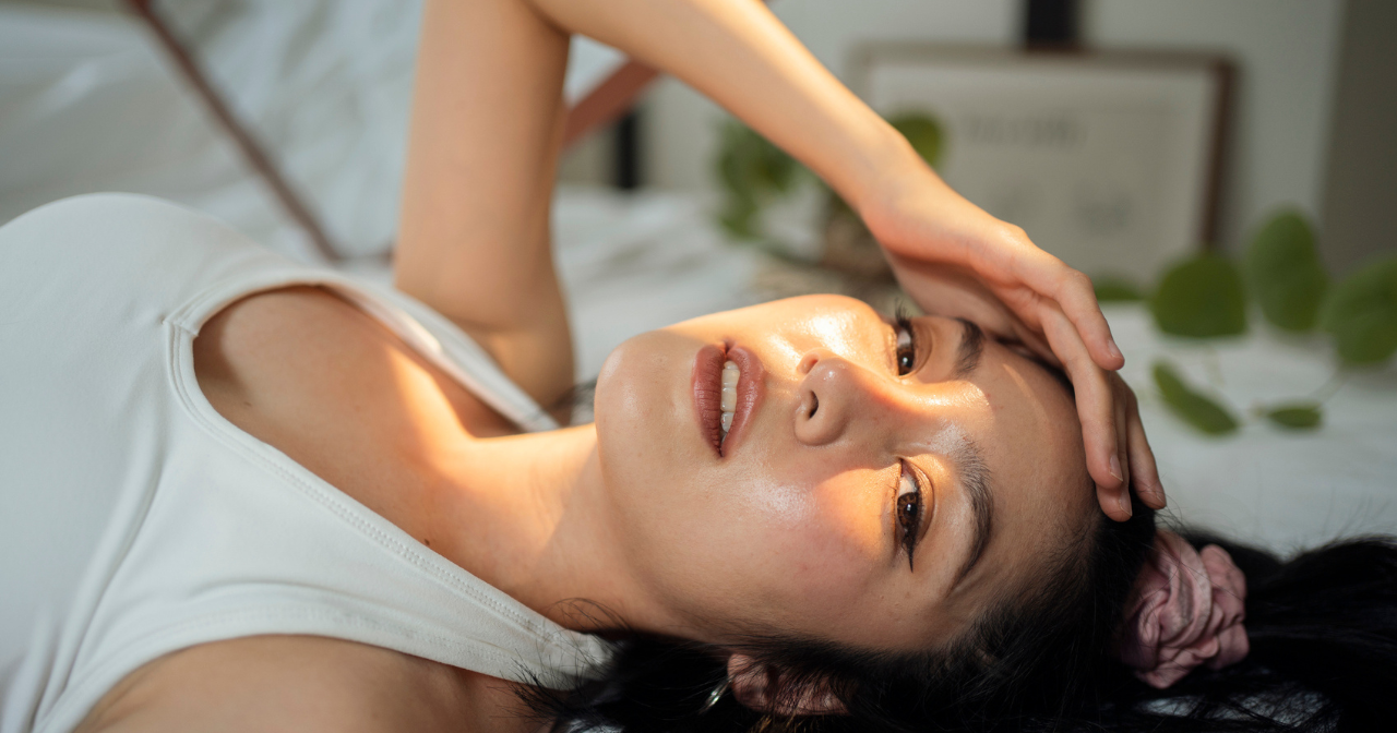 An Asian woman lays down with a hand shading her eyes from the sun.