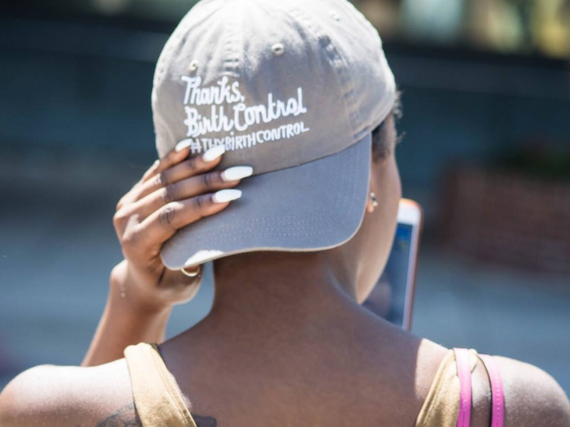 A Black woman wears a hat backwards that reads, "Thanks, Birth Control" 
