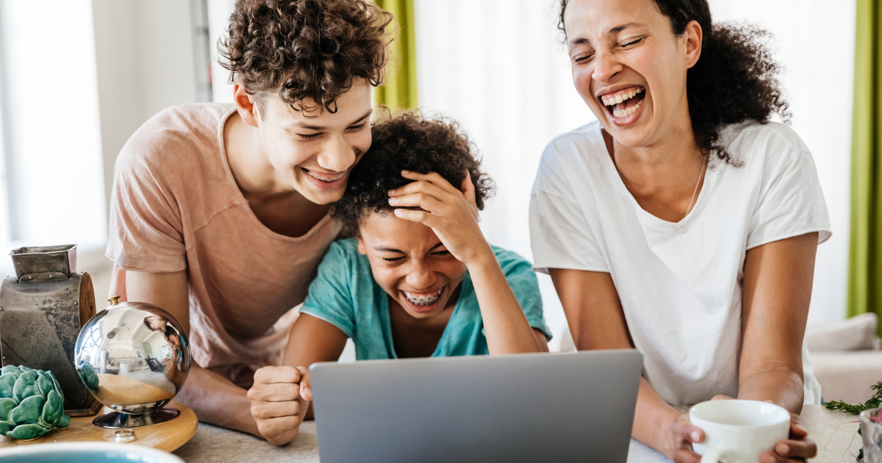 A mom and her two kids laugh while looking at a computer. 