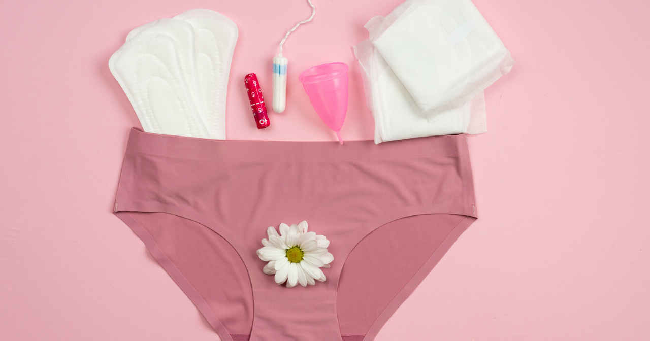 A pair of underwear lay spread out against a pink background with a number of period products scattered around. 