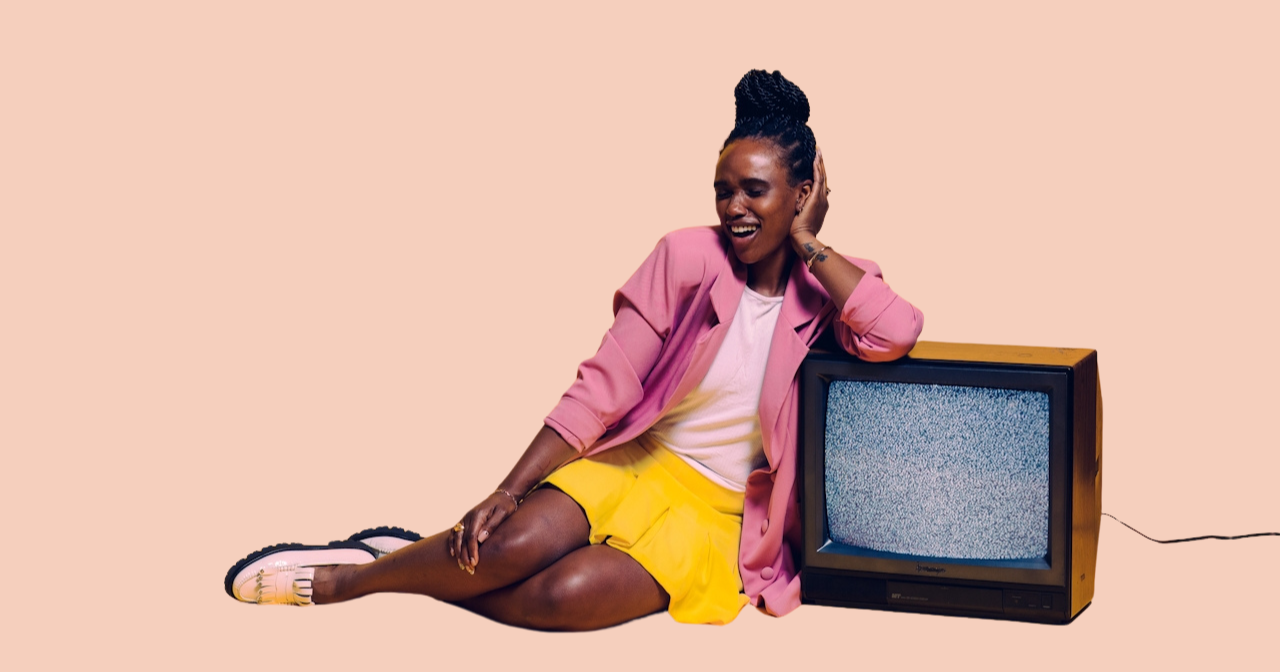 A Black woman leans against a TV and smiles. 