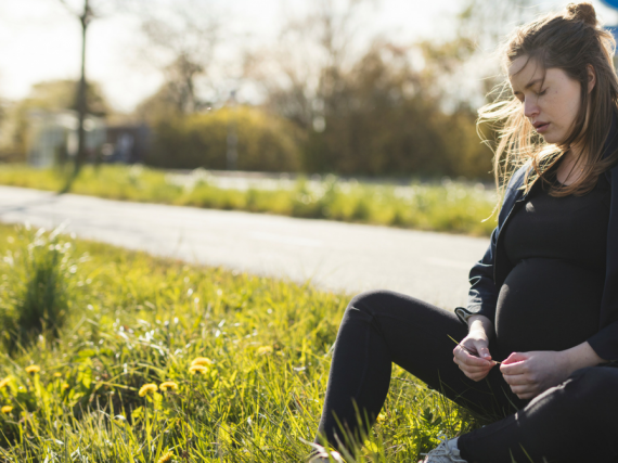 A pregnant woman sits by a road