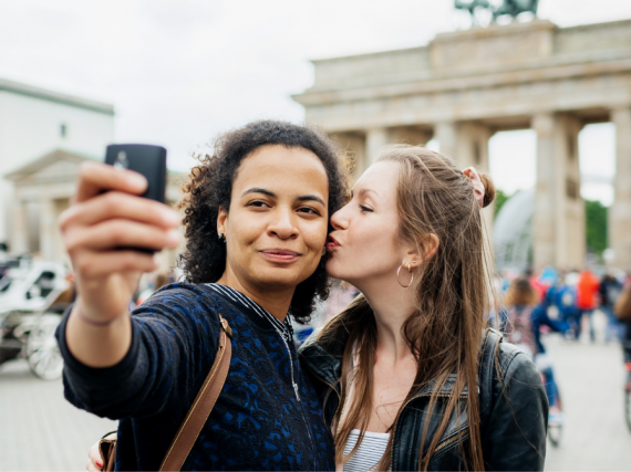 A woman kisses her girlfriend's cheek as they take a selfie