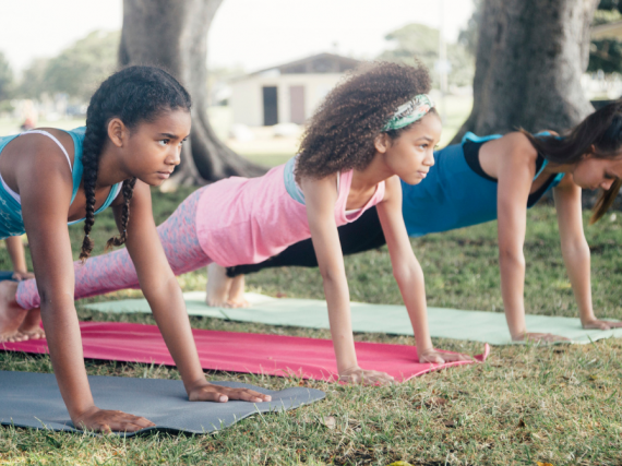 Three young girls do yoga outdoors