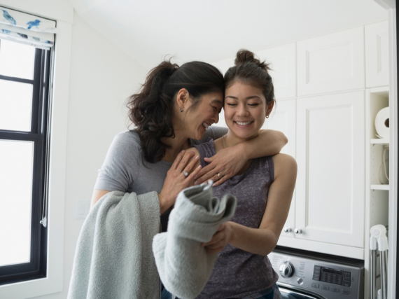 A mother hugs her teen as she folding laundry.
