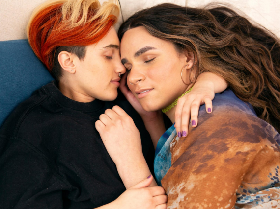 A gender nonbinary/trans couple lay in bed together and snuggle. 