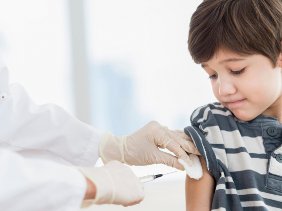 A young boy looks down as he is vaccinated by a provider. 