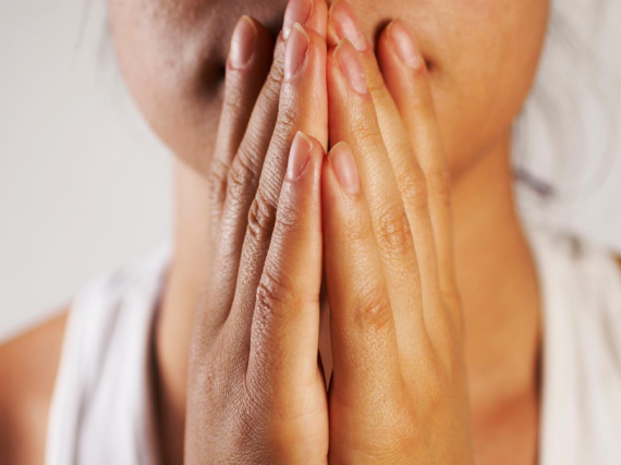 A close up of a woman's hands covering her mouth in a worried fashion. 