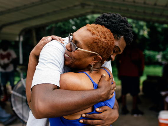 A Black woman hugs her son outdoors. 