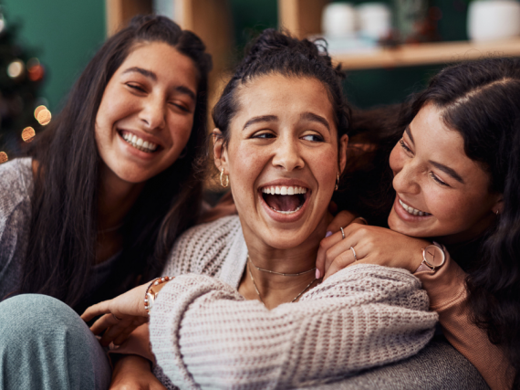 Three sisters laugh in their living room. 