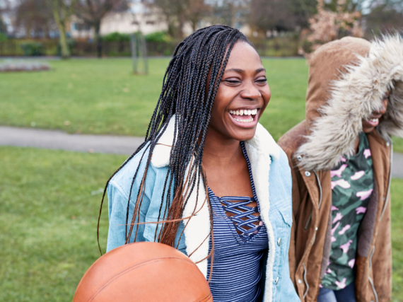 Two Black girls laugh while walking through a park.