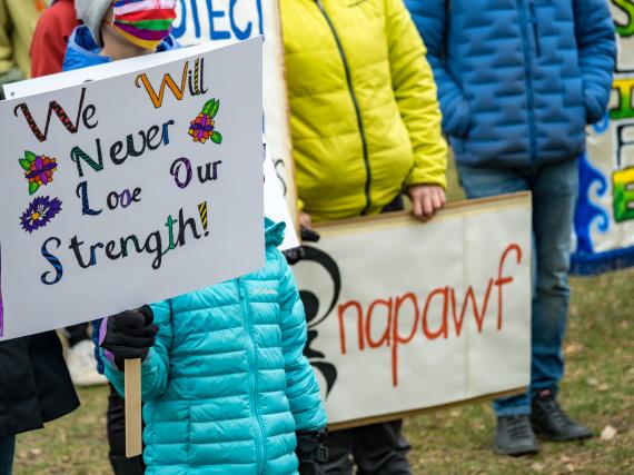 A photo of people holding signs that read, "We will never lose our strength!" and "NAPAWF"
